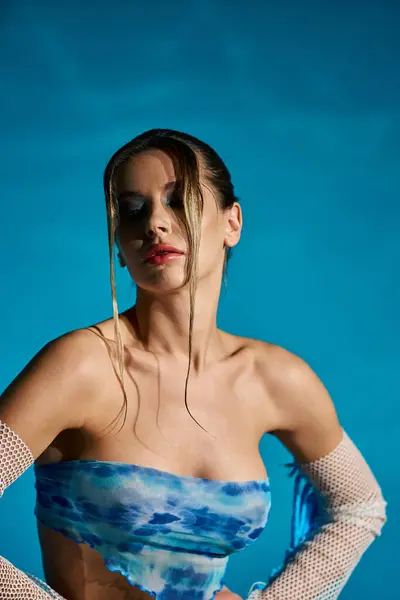 Une jeune femme dans un haut de culture bleu à la mode pose au bord de l'eau sur un fond bleu. — Photo de stock